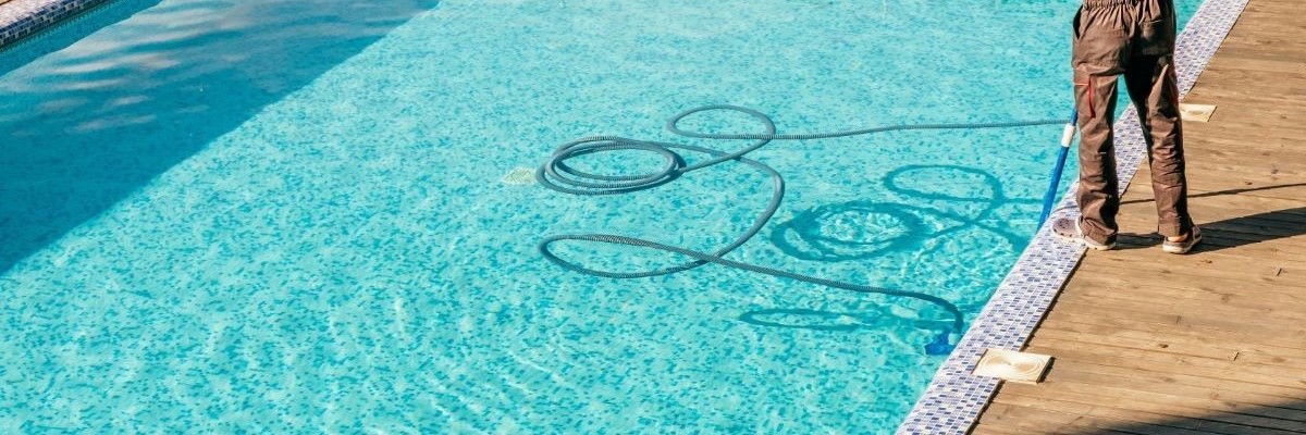 Jupiter Island Pool Services by Jupiter Island Pools a man is vacuuming a pool that has several small square subway tiles as the coping and pool bottom in blue, light blue and whites colors